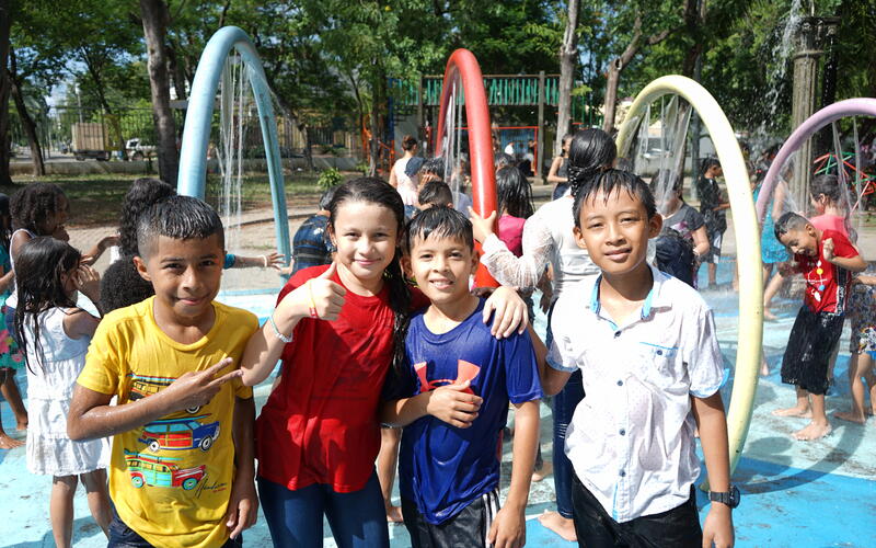 In Honduras, four children stand together in a splash pad and smile