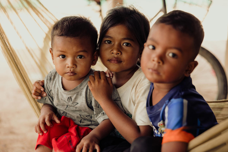 In Cambodia, three children shelter in a tent, sitting close together. 