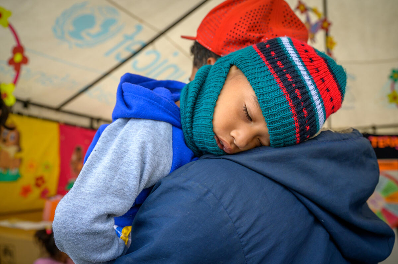The father of two-year-old Jhaverson carries him into a shelter for asylum seekers in Colombia. The family has fled from Venezuela, along with one in every four citizens.
