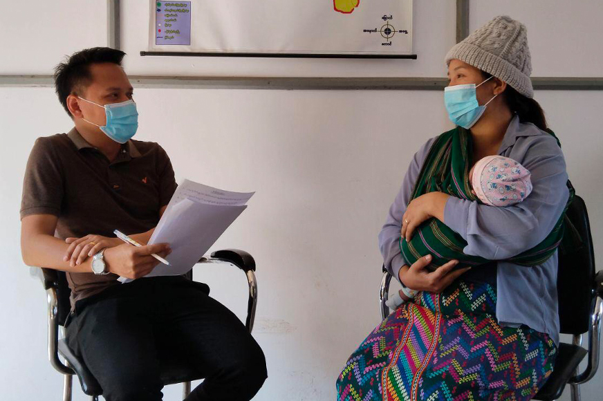 A man and a woman cradling a baby wears a facemask in a clinic. 