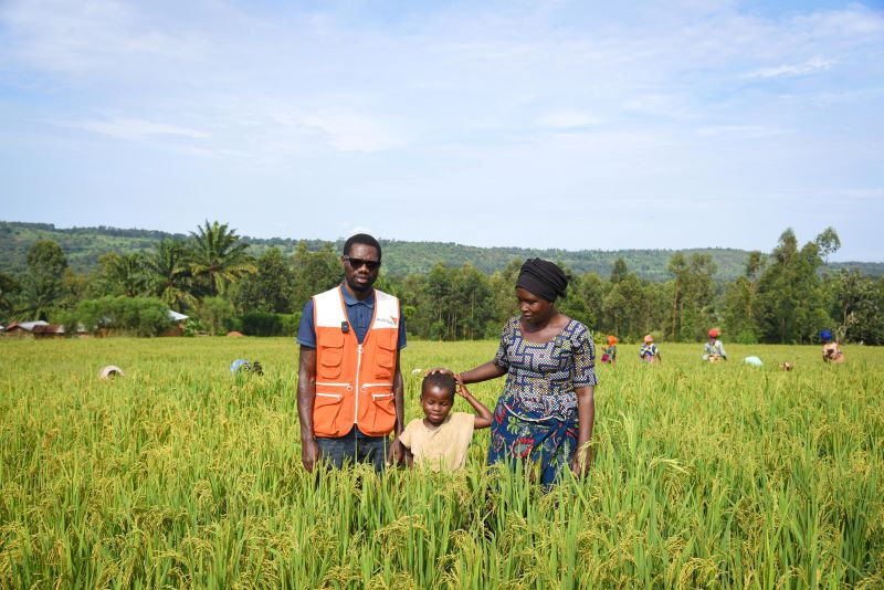 In the Democratic Republic of the Congo, local staff member stands in a lush field with Magnifique (5) and her mother, Odette.