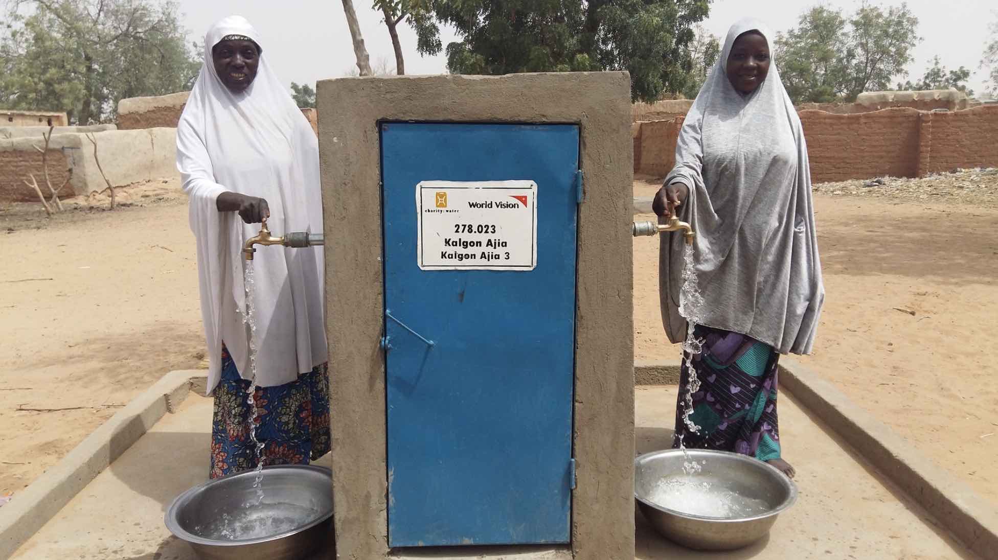 Two women collect water in basins after the construction of water pipes in their village.