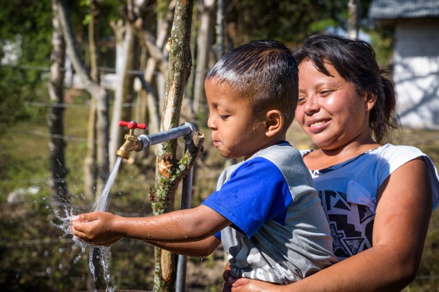 Johanna Hernandez, 23, holds her son David, 5, so he can wash his face and drink clean water flowing from one of the taps in Jamastran ADP, built by the community with funding from World Vision US and major donor, Refined Technologies, based in Texas.