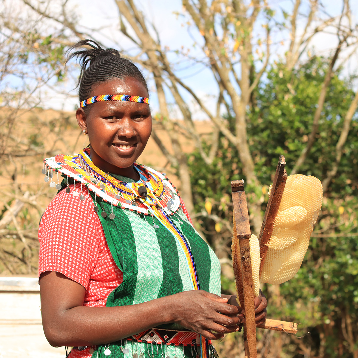 A woman smiles as she holds honeycombs from her recent honey harvest from her beehives.