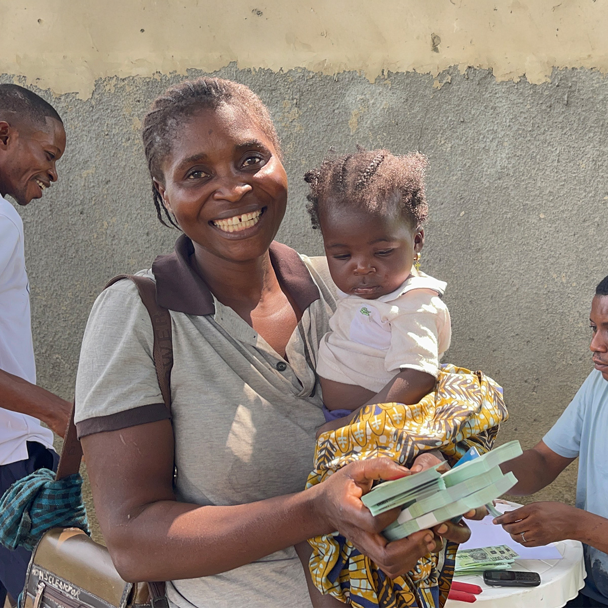 A smiling mother holds her baby in one arm, and cash in another.