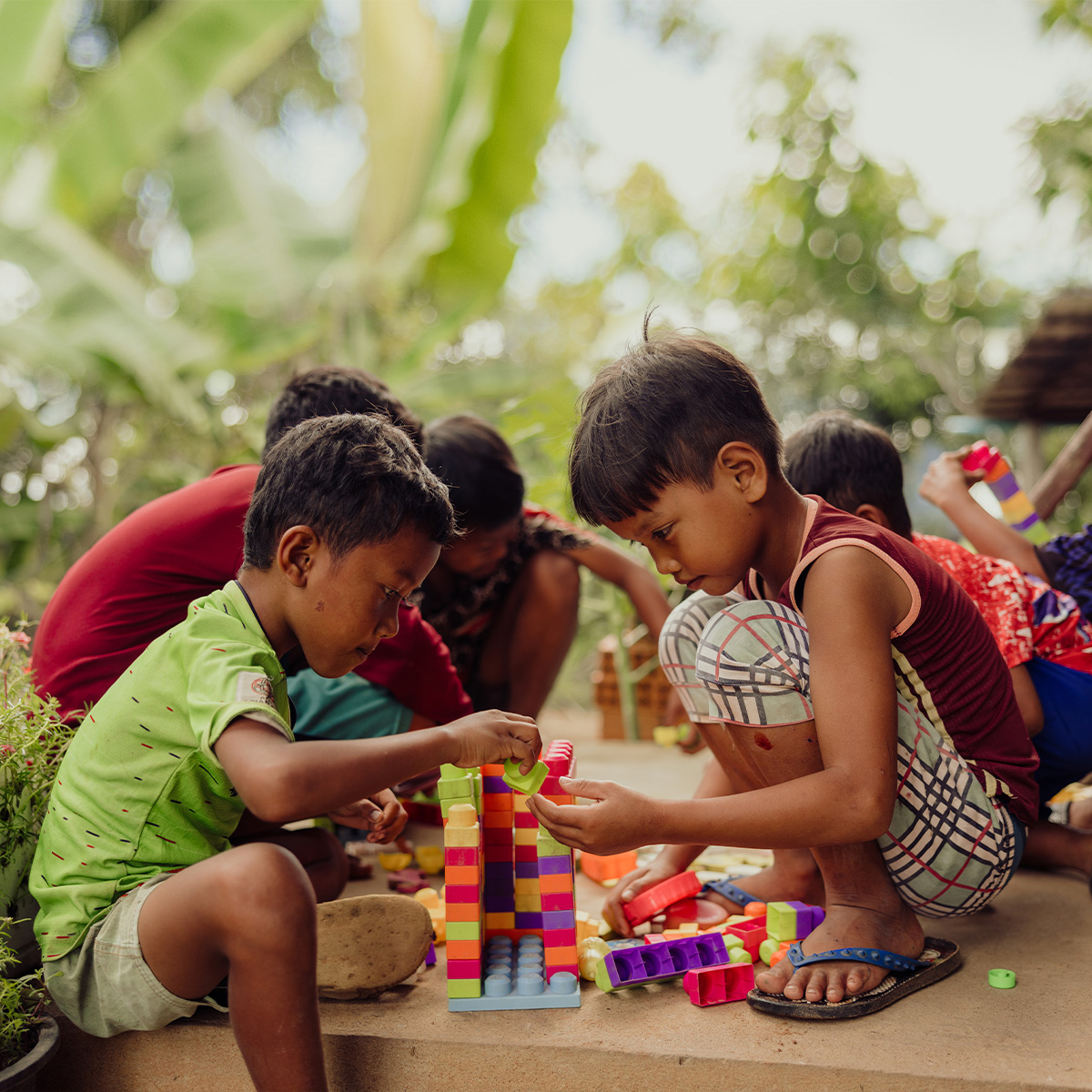 A group of boys kneel on the ground, playing with colourful blocks.