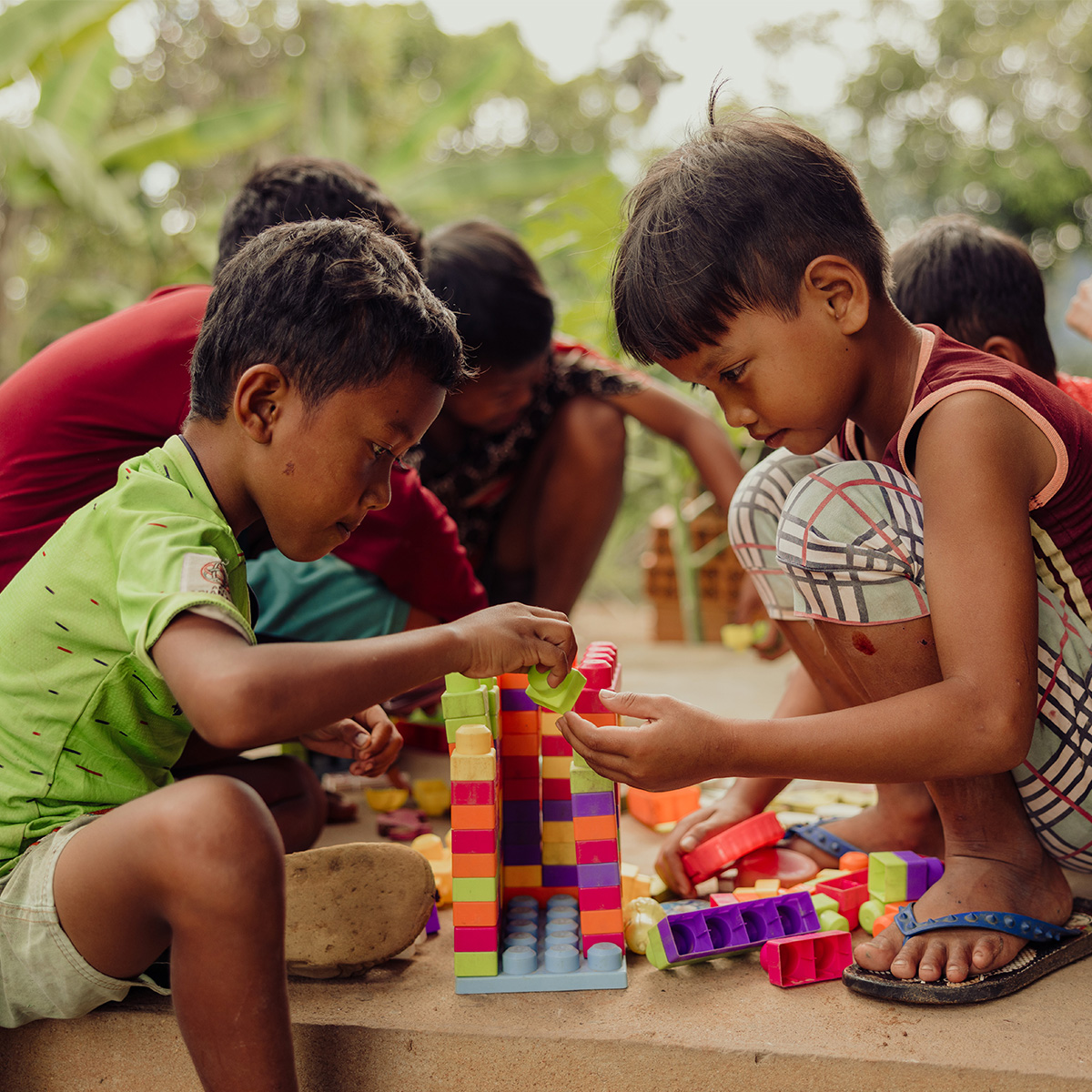 A group of boys kneel on the ground, playing with colourful blocks.