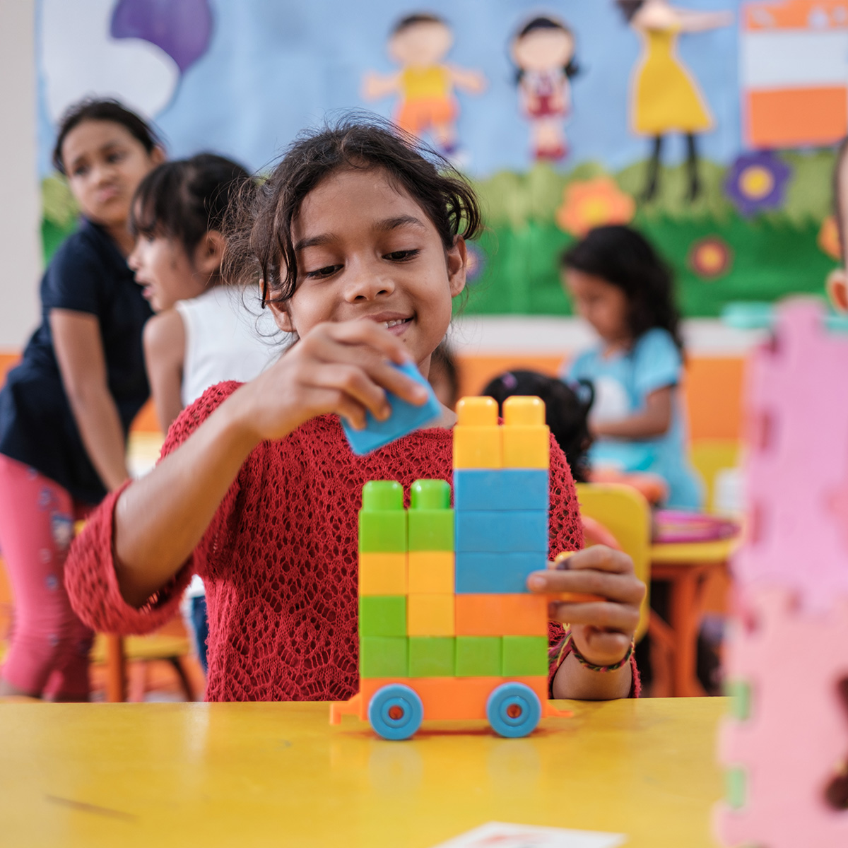 A young girl stacks colourful blocks in a classroom.