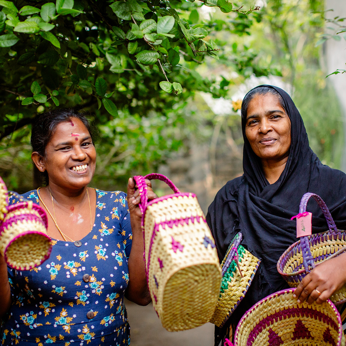 Two smiling women hold up handmade, colourful woven baskets towards the camera.