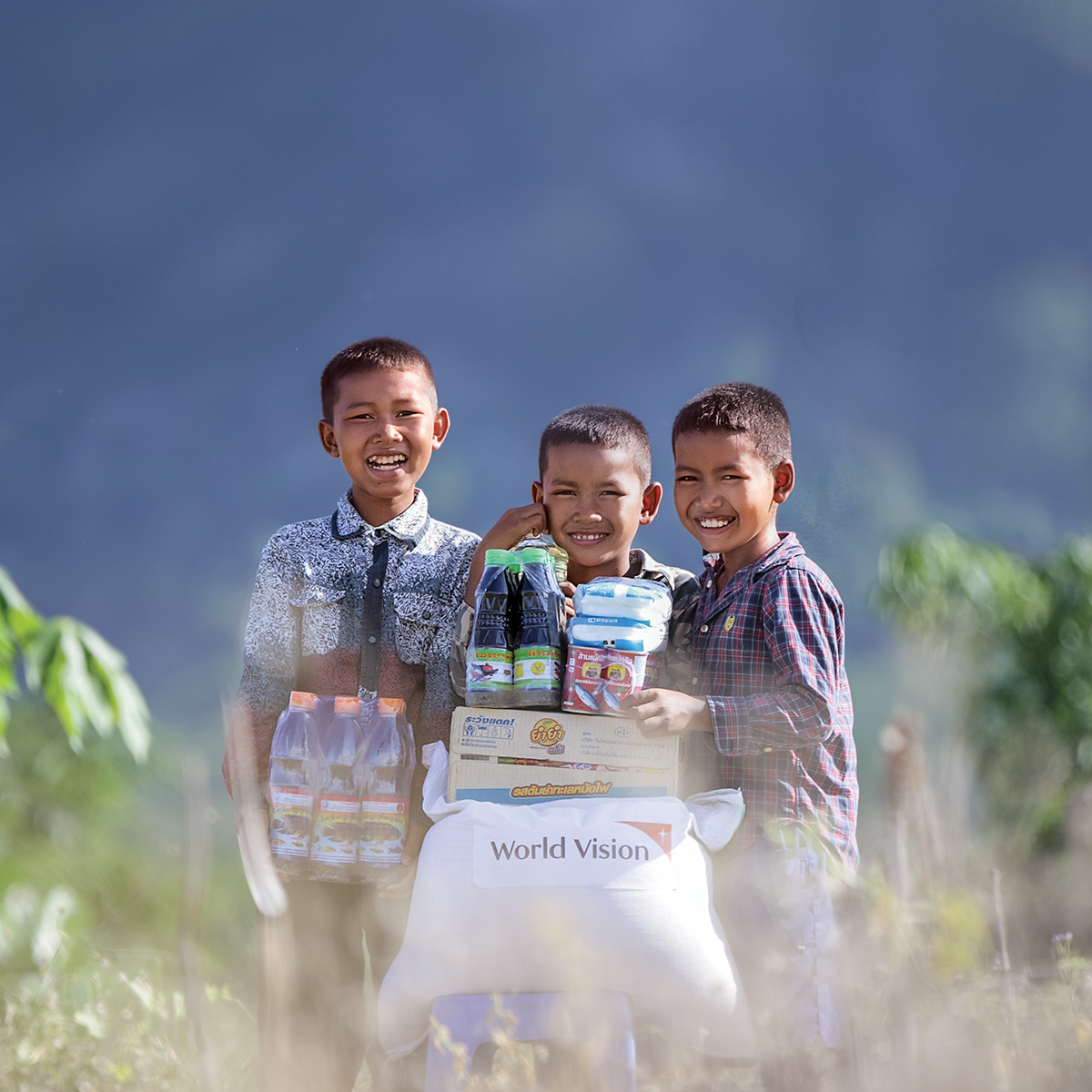 Three boys smile next to each other as they stand behind a pile of food items.