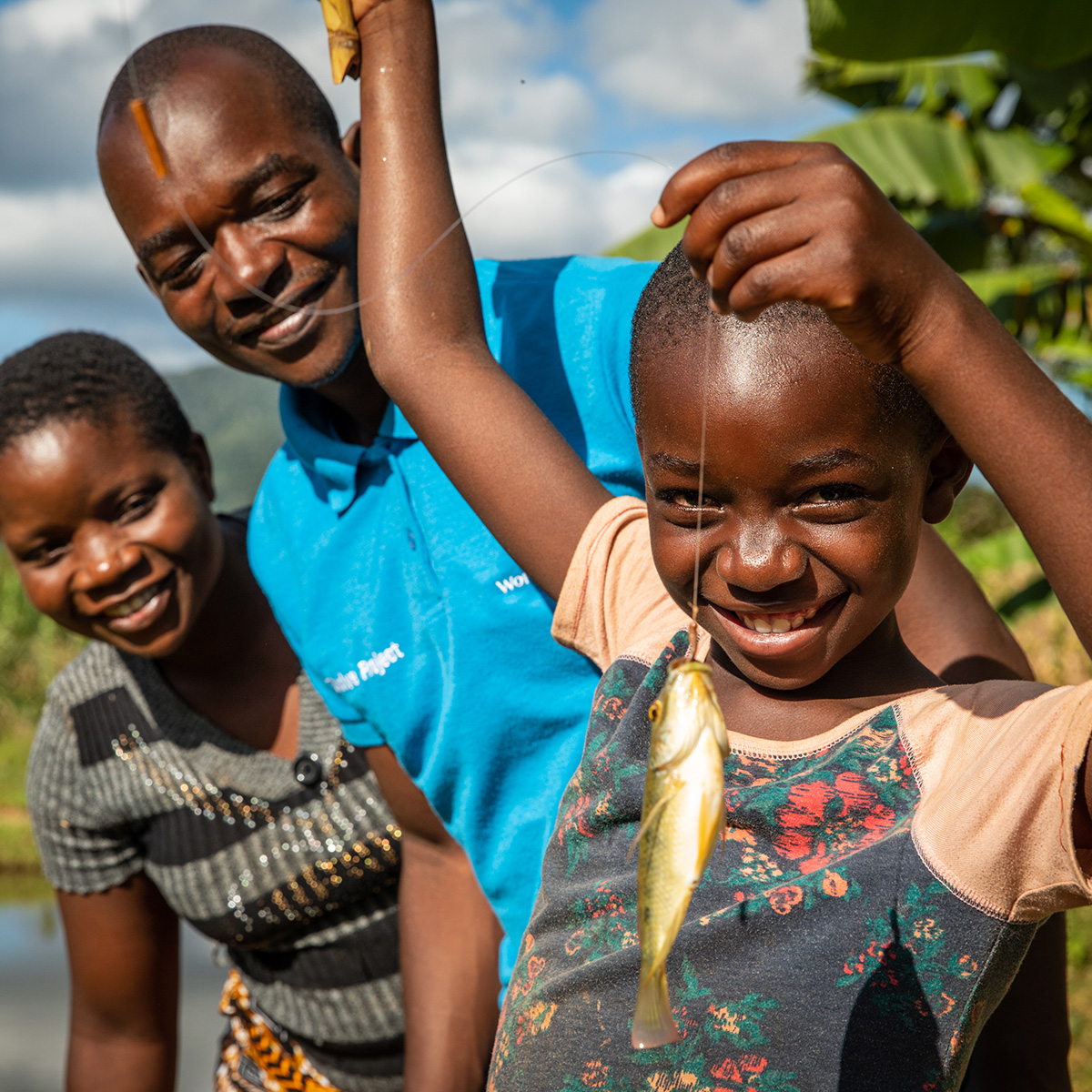  A smiling child dangles a fish from a string, while his parents stand behind him.