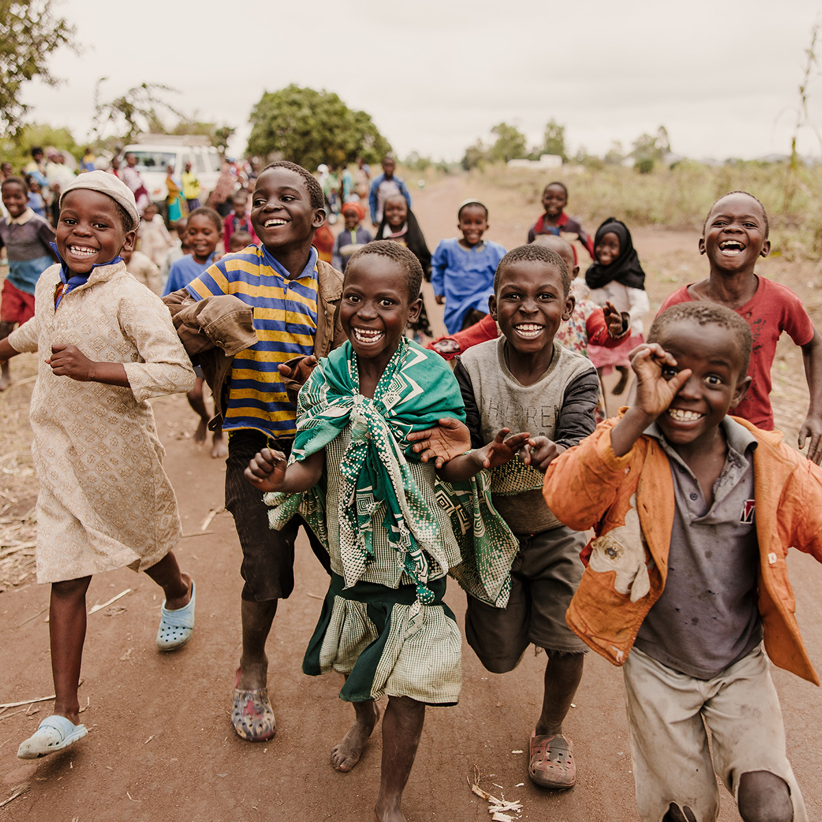 Dozens of children run down a dirt road, smiling and laughing.