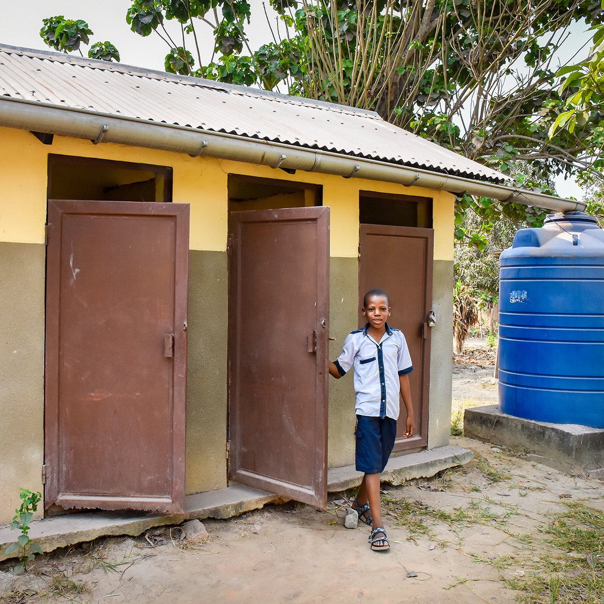 A young boy in a blue uniform exists a newly built school latrine.