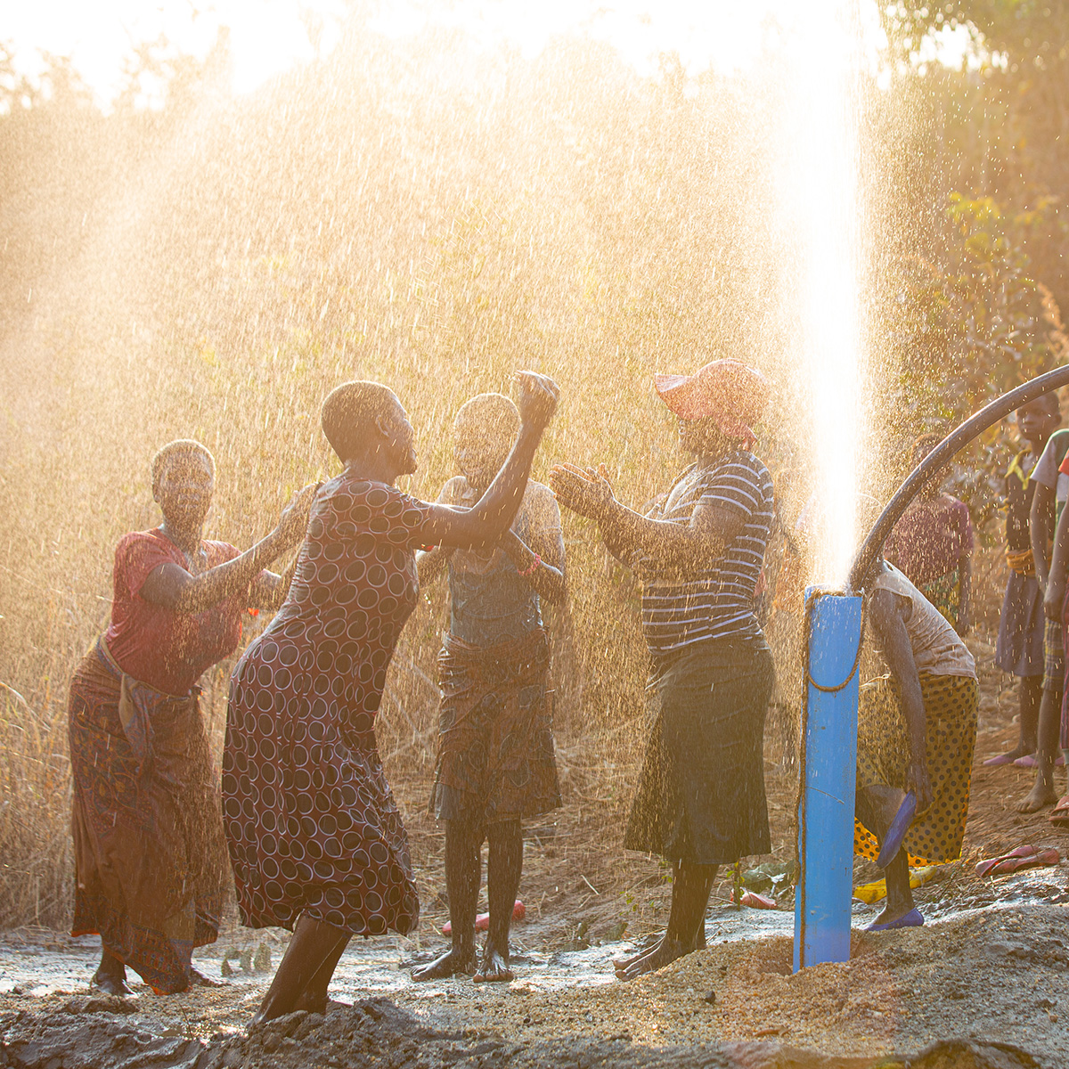 Women and elders dance beneath showers of water from a newly drilled borehole as children watch on.