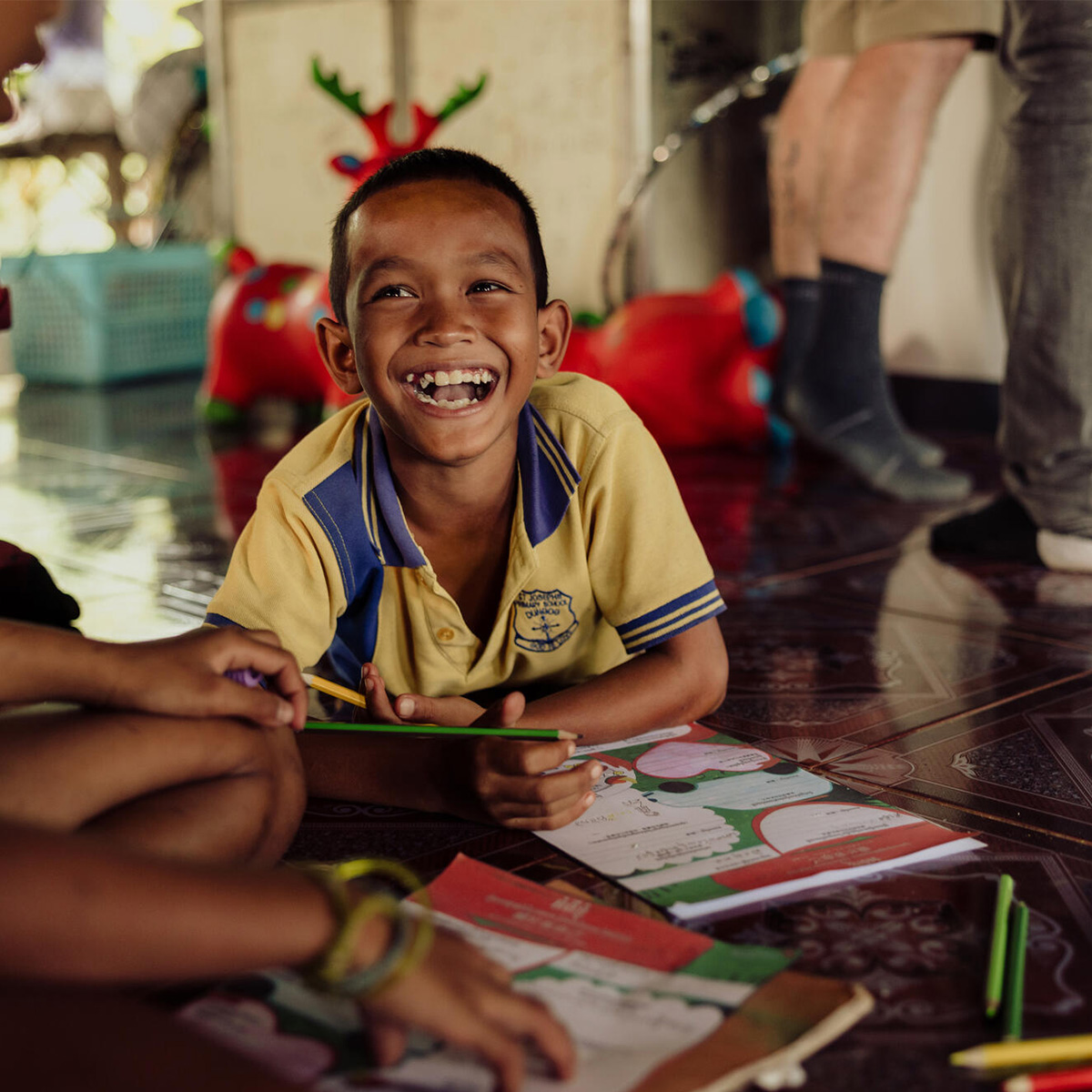 A boy smiles towards his friend, while using colouring pencils for an activity.