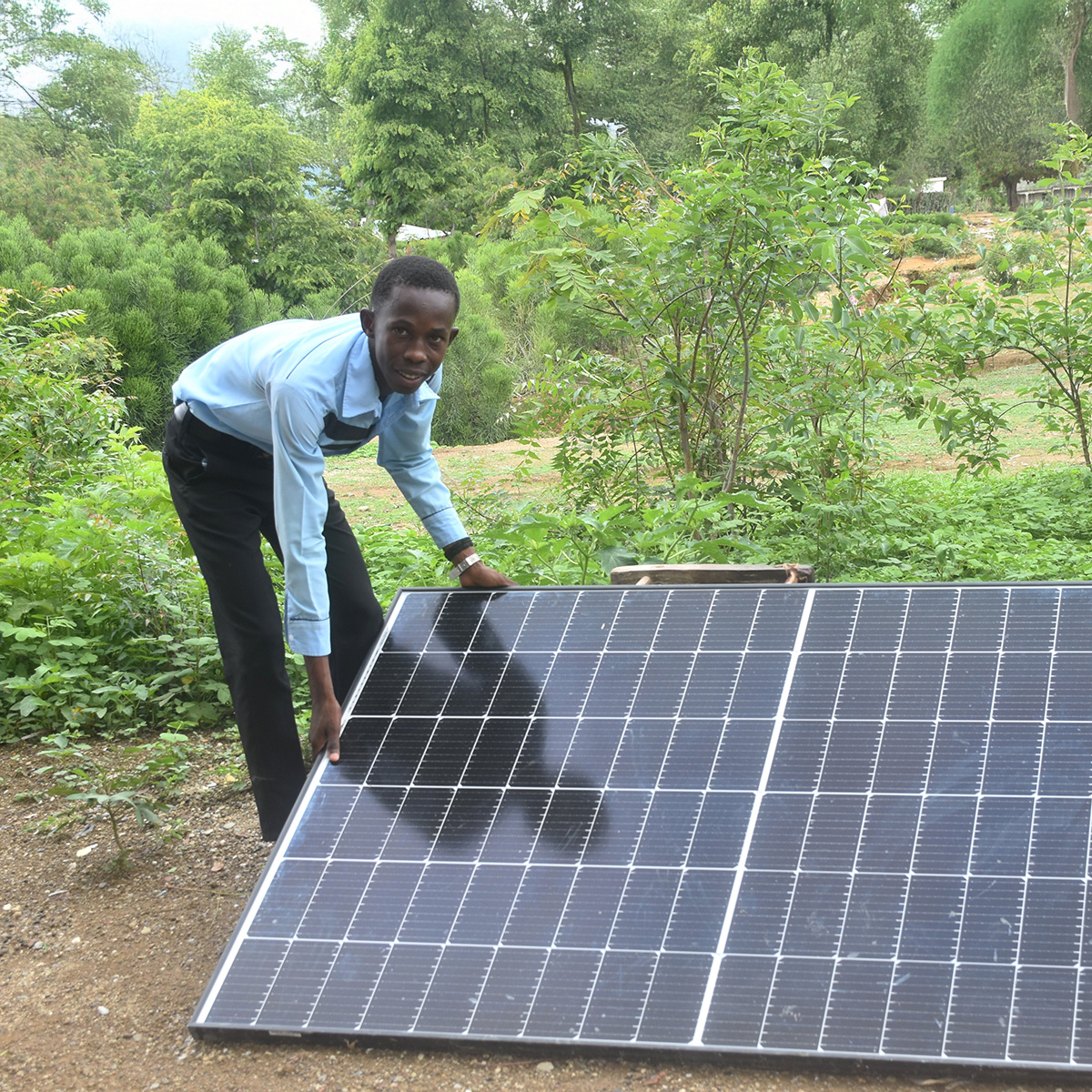 A boy in a rural setting bends over, adjusting a solar panel.