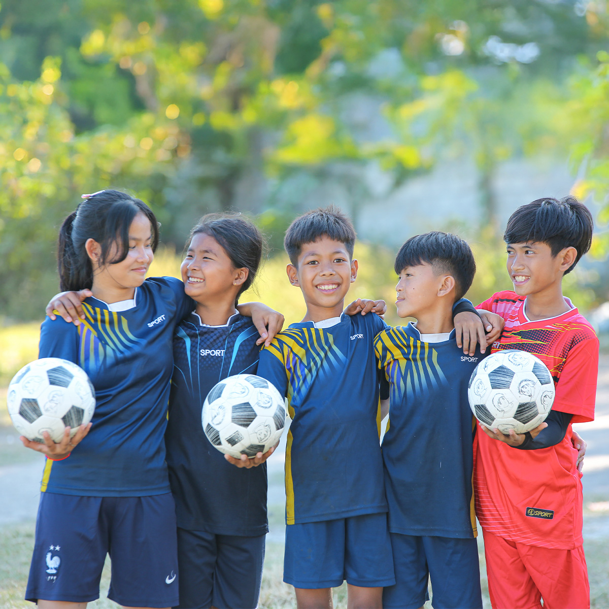 Group of children in sports uniforms holding soccer balls outdoors.