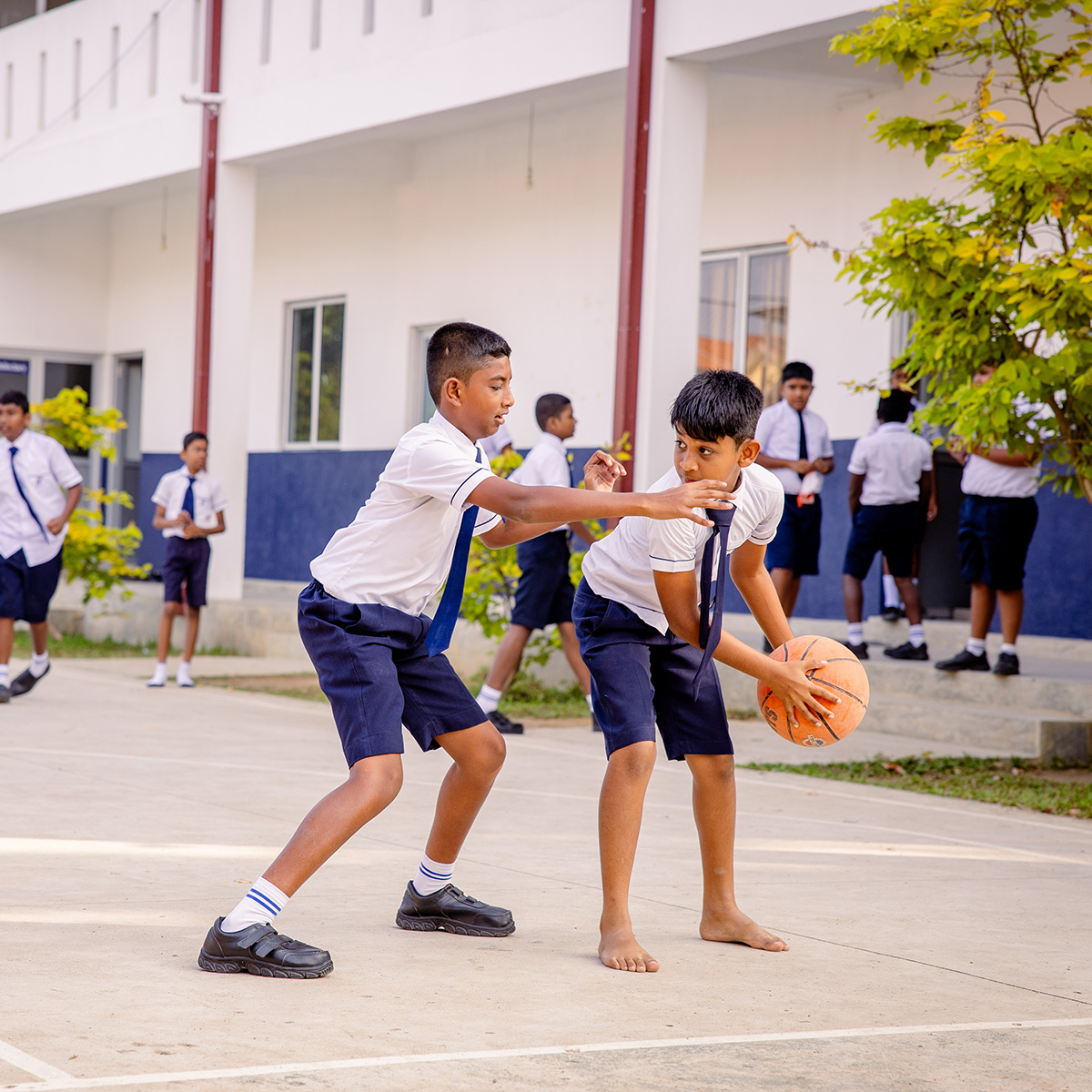 Two boys in uniform play blasketball outdoors in front of a school.