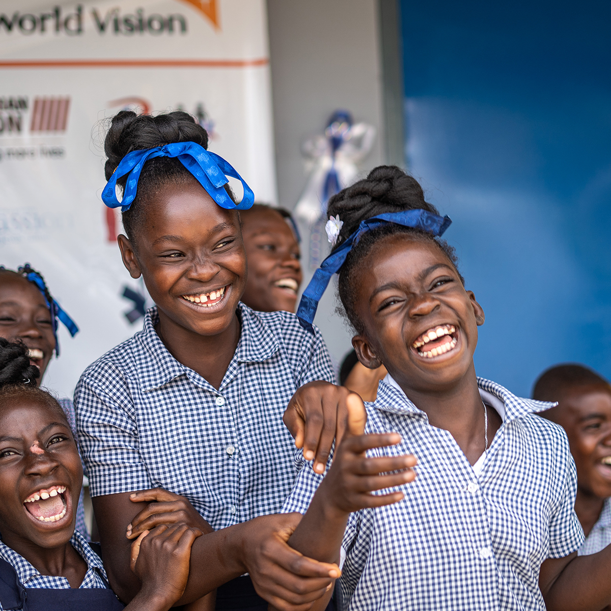 School girls wearing blue uniforms and blue hair ribbons laugh together.