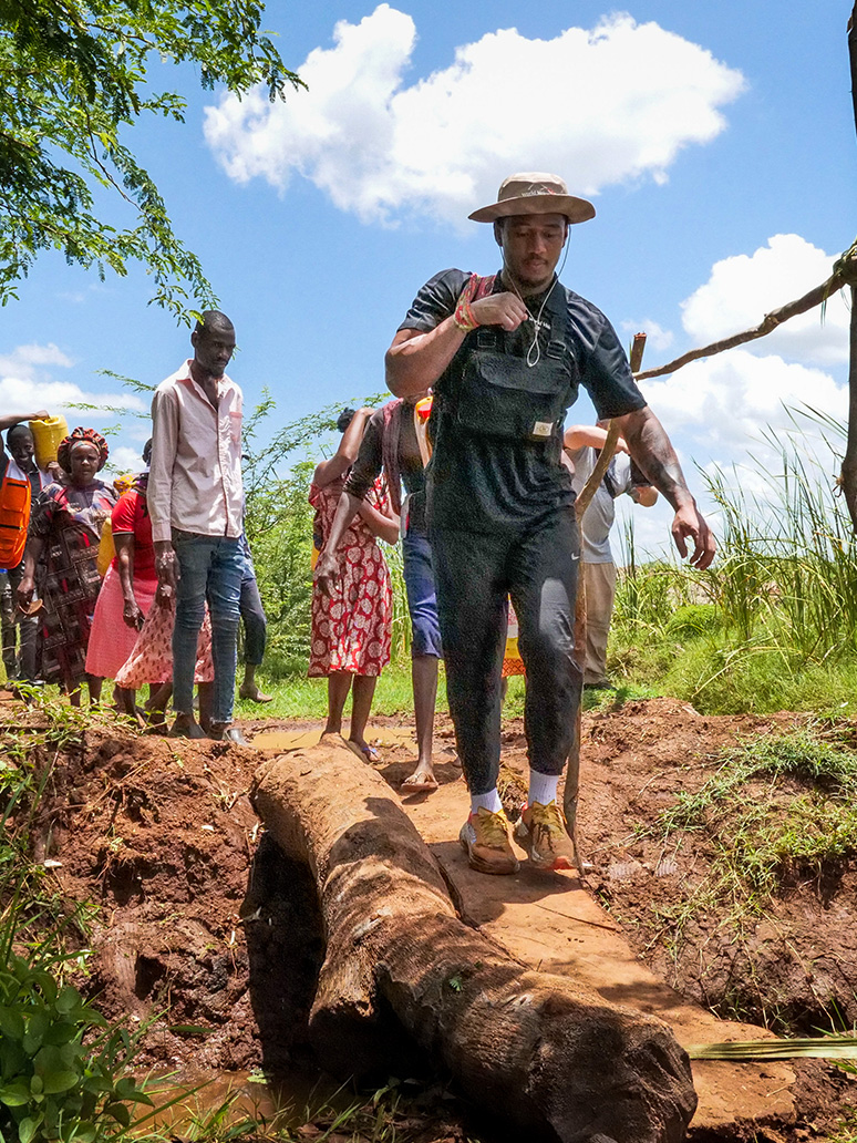 A CFL player walks along a trail at the front of a line of people, while carrying a yellow bucket.