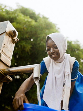 A young girl fills up a blue bucket with water.