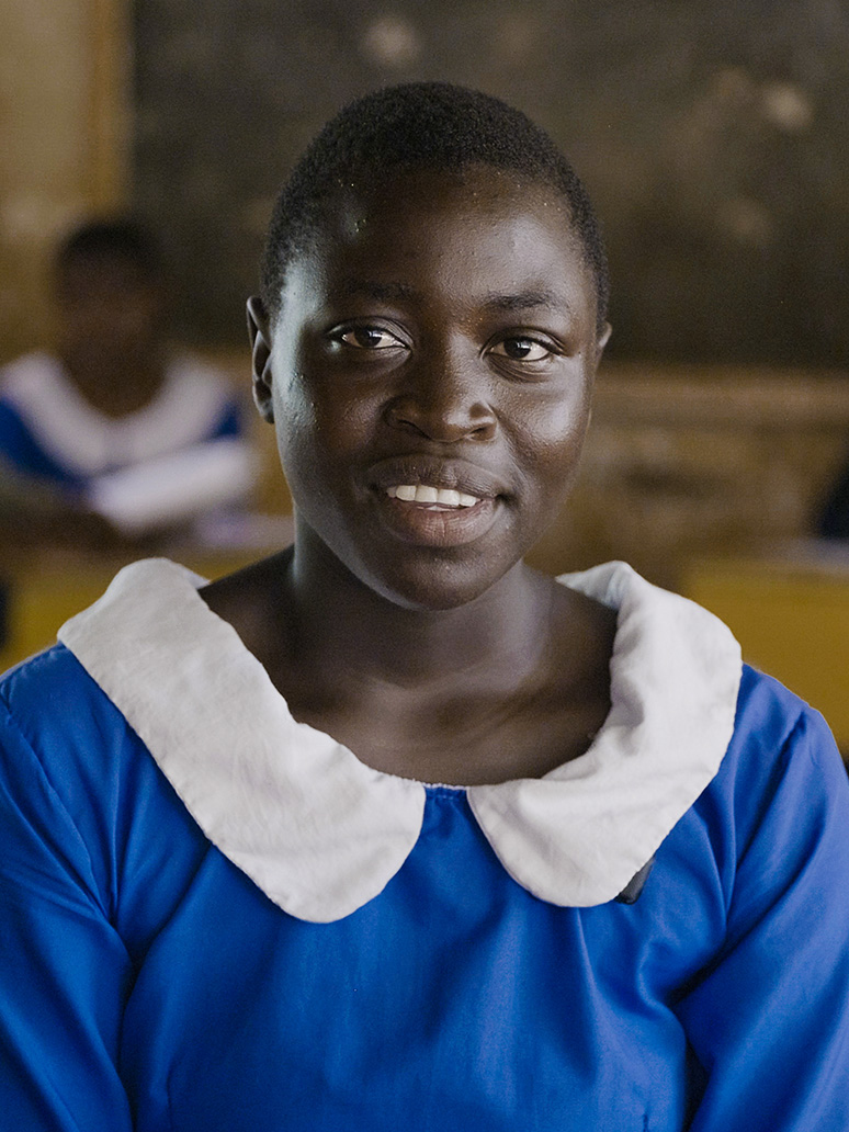 A teenage girl in a blue and white school uniform, smiles.