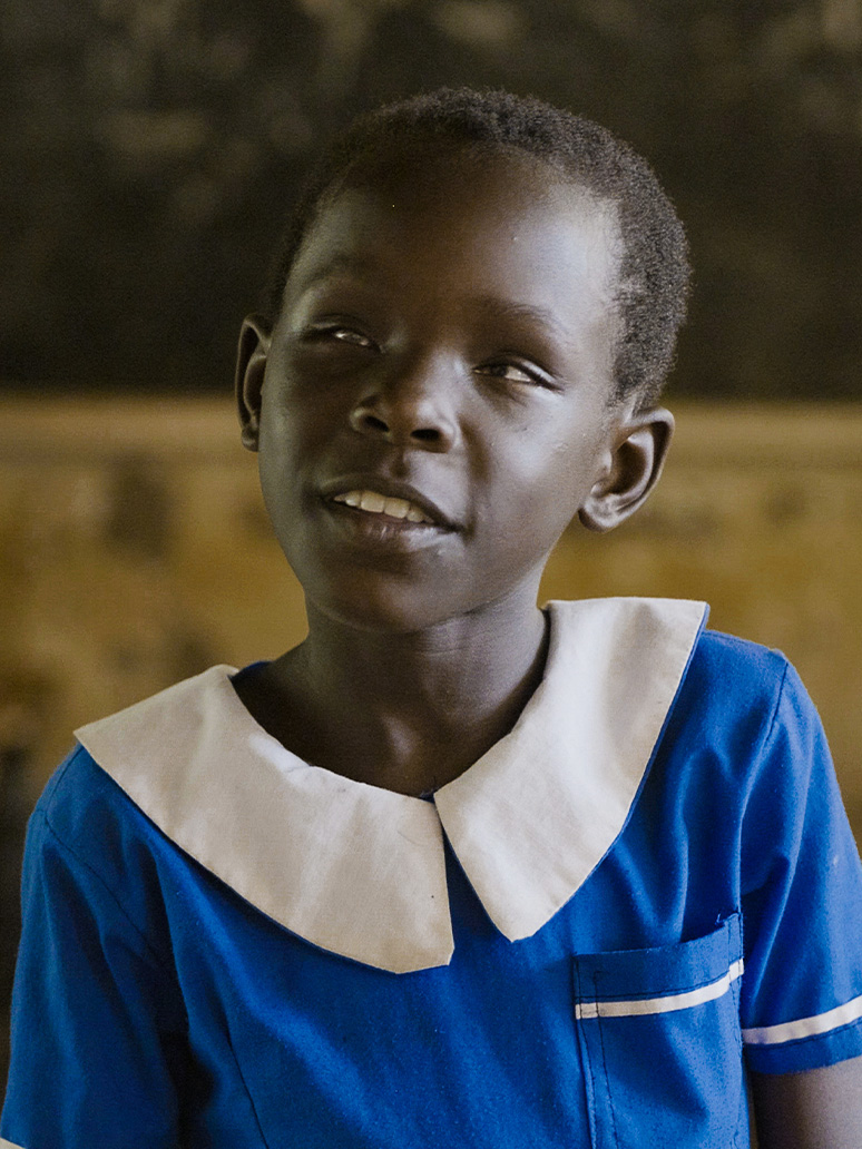 A young girl in a blue school uniform, smiles.