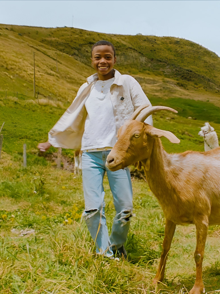 A young boy dances with a goat in a field.